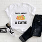 White t-shirt with black writing that says Taco About A Cutie. In the middle is a smiling Taco