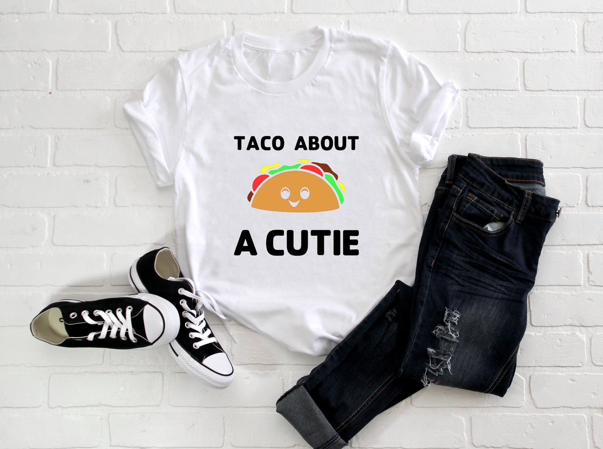 White t-shirt with black writing that says Taco About A Cutie. In the middle is a smiling Taco
