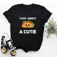 Black t-shirt with white writing that says Taco About A Cutie. To this middle is  a brown smiling Taco.