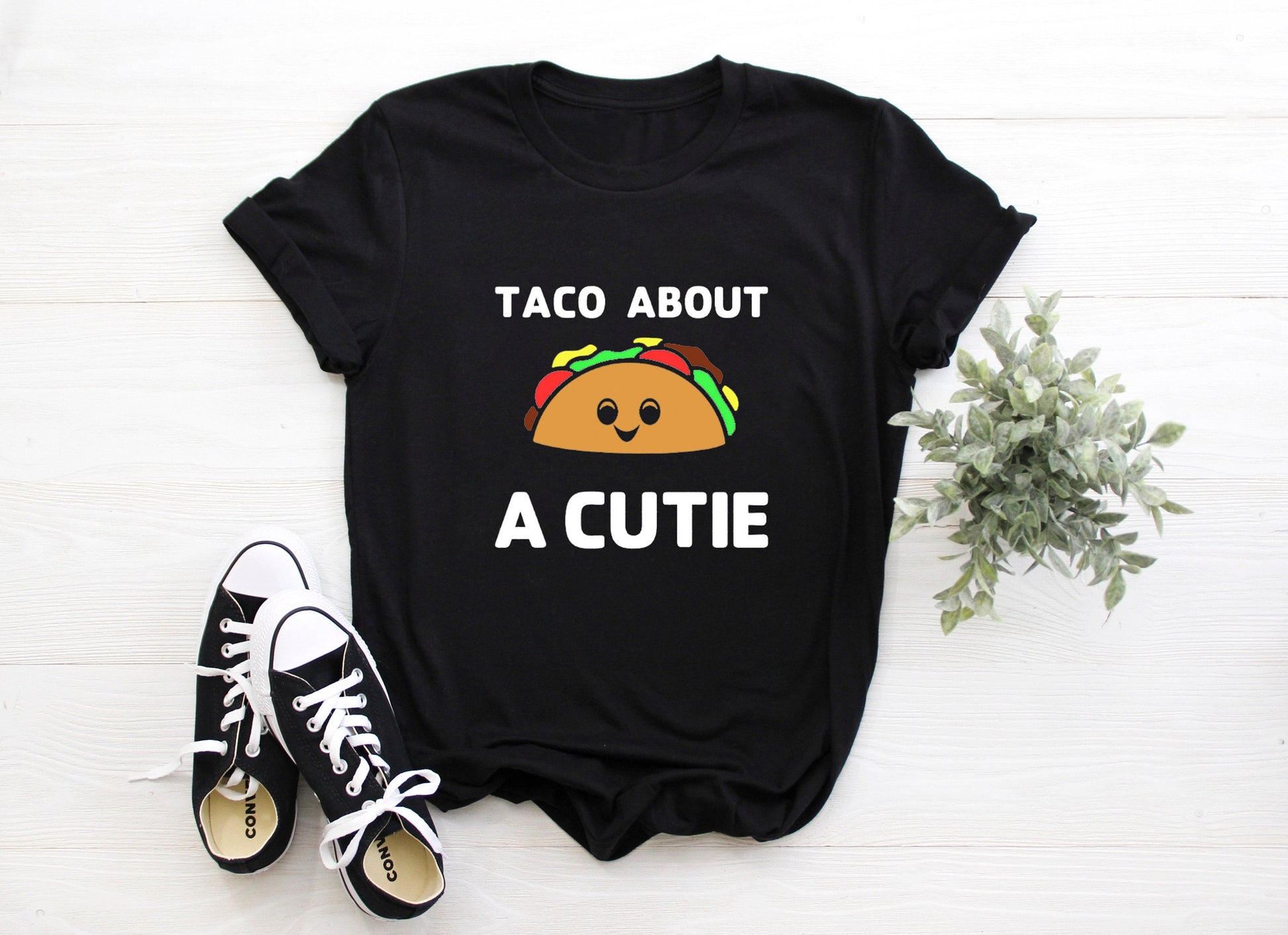 Black t-shirt with white writing that says Taco About A Cutie. To this middle is  a brown smiling Taco.